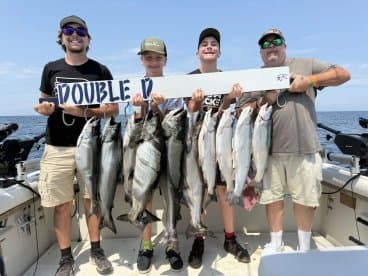 A group of four anglers proudly displaying their catch of multiple Salmon on a fishing charter, showcasing a successful day on the water.