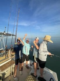 A group of excited anglers, including children and adults, proudly displaying their catch of several fish while enjoying a sunny day on the water.