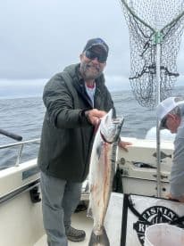 An angler proudly displaying a large Salmon aboard a fishing boat, showcasing a successful day on the water.