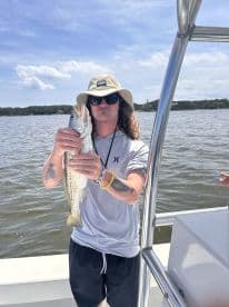 Angler proudly displaying a Speckled Trout while fishing from a boat in a coastal waterway.