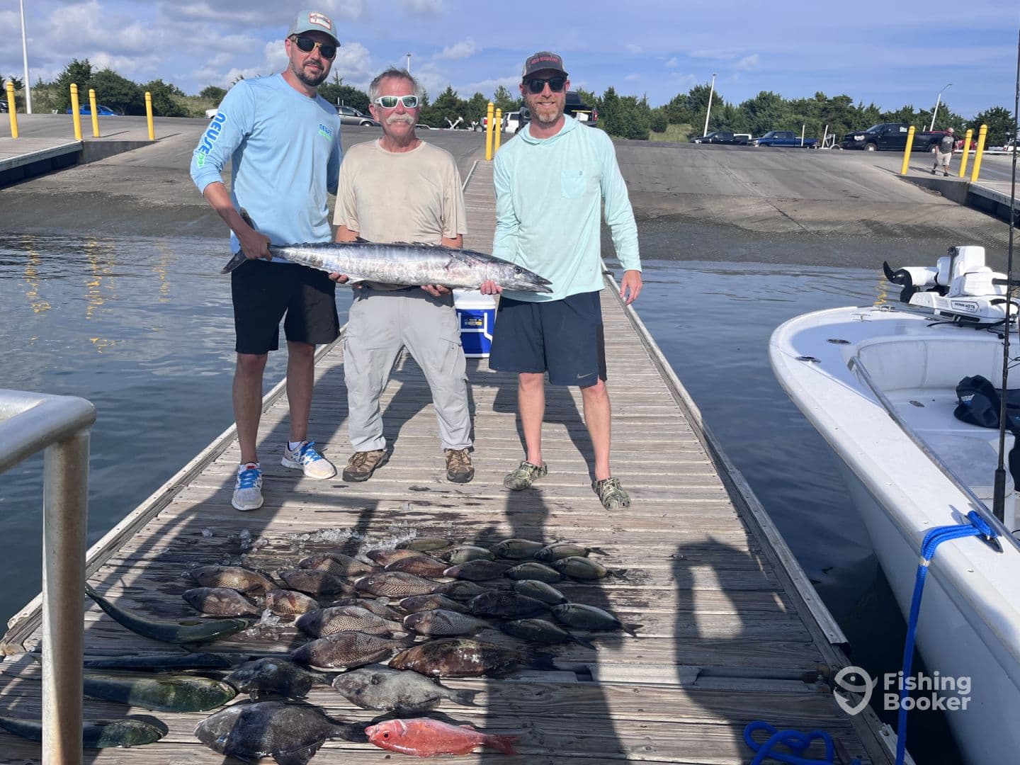 Three anglers proudly displaying a large Wahoo alongside a variety of fish caught during a successful fishing trip at the dock.