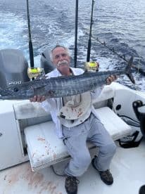 An angler proudly displaying a large Wahoo on a fishing boat, showcasing the excitement of deep-sea fishing.