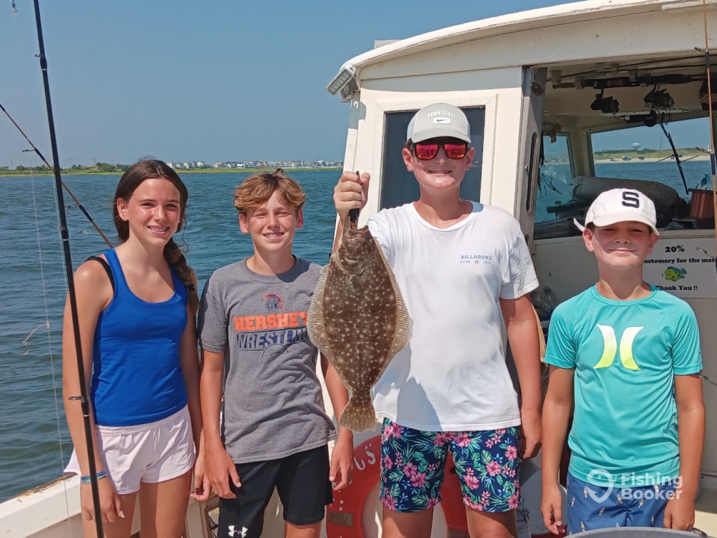 A group of young anglers proudly displaying a Flounder caught during a fun day of fishing on a boat.