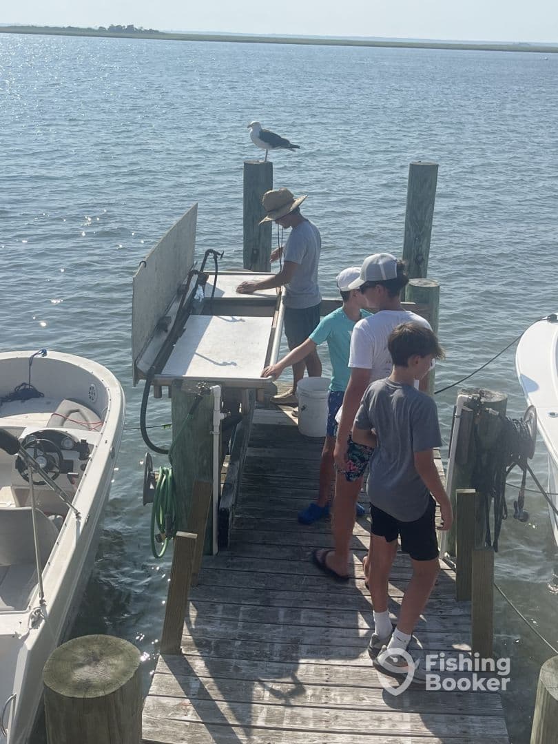 A group of young anglers gathered at a cleaning station on a dock, preparing their catch after a day of fishing in a coastal environment.
