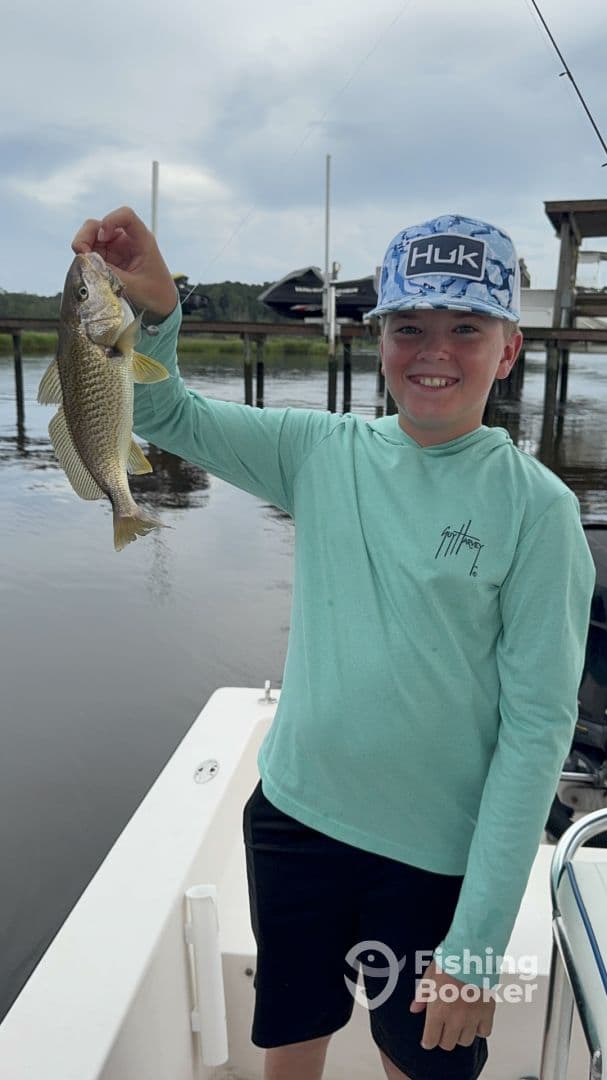 A young angler proudly displaying a caught fish while on a boat, showcasing a fun day of fishing in a calm water environment.