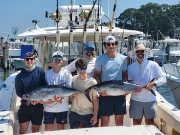 A group of young anglers proudly displaying their catch of large Bluefin Tuna aboard a sport fishing boat at the marina.