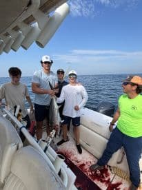 A group of young anglers proudly displaying a large Tuna on a sport fishing boat, showcasing their successful catch during a day on the water.