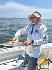 An angler proudly displaying a caught shark while fishing from a boat in open waters.