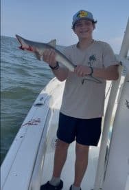 Young angler proudly holding a small shark while fishing on a boat, showcasing a successful catch in a coastal environment.