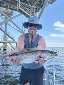 Angler proudly displaying a Speckled Trout while fishing near an offshore platform.