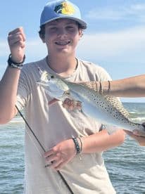 A young angler proudly displaying a Speckled Trout while fishing on a sunny day, showcasing the excitement of a successful catch.