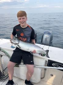 A young angler proudly displaying a large Salmon while fishing on a boat in open waters.