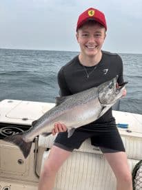 A young angler proudly displaying a large Salmon while fishing on a boat, showcasing a successful catch in open waters.