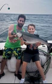A young boy and an adult proudly displaying a large Salmon while fishing on a boat, showcasing a memorable family fishing experience.