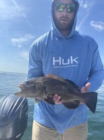 Angler holding a large Grouper while fishing in clear waters, showcasing a successful catch during a day on the boat.