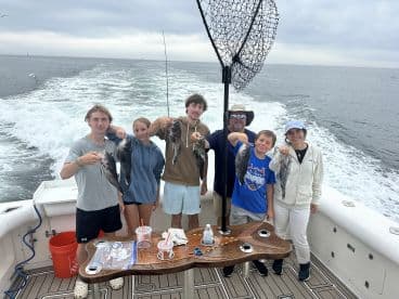 A group of young anglers proudly displaying their catch of Black Sea Bass aboard a fishing charter, enjoying a day on the water.