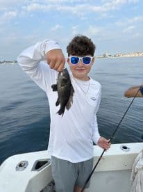 A young angler proudly displaying a Black Sea Bass while fishing on a boat, showcasing a successful day on the water.