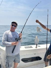 Angler enthusiastically reeling in a Flounder while fishing on a boat, showcasing the excitement of a successful catch.
