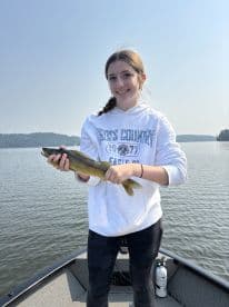 A young angler proudly displaying a Walleye while fishing from a boat, surrounded by calm waters.