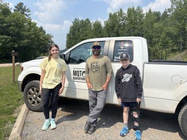 A family poses by their truck, ready for an outdoor adventure, showcasing a friendly atmosphere and excitement for fishing.