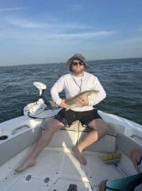 An angler proudly displaying a large Redfish while seated on a boat in a coastal fishing environment.