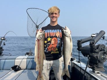 Young angler proudly holding two Lake Trout while fishing on a boat in open water.