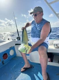 An angler proudly displaying a vibrant Mahi Mahi aboard a fishing boat in open waters, showcasing a successful deep-sea fishing trip.