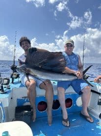 A young angler and an adult proudly displaying a large Sailfish on a fishing boat, showcasing their successful catch during a deep-sea fishing trip.