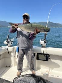 An angler proudly displaying a large Salmon aboard a fishing boat, surrounded by a scenic lake view.