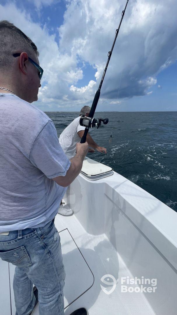 Two anglers actively fishing on a boat, with one reeling in a catch while enjoying a day on the water.