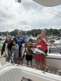 A family group proudly displaying their catch of striped bass at the marina, showcasing a successful day of fishing.
