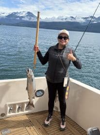 Angler proudly displaying a large Salmon while fishing in a scenic coastal environment, surrounded by mountains.
