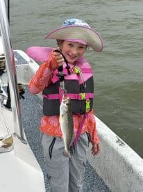 Young angler proudly displaying a Speckled Trout while fishing from a boat, showcasing a fun day on the water.