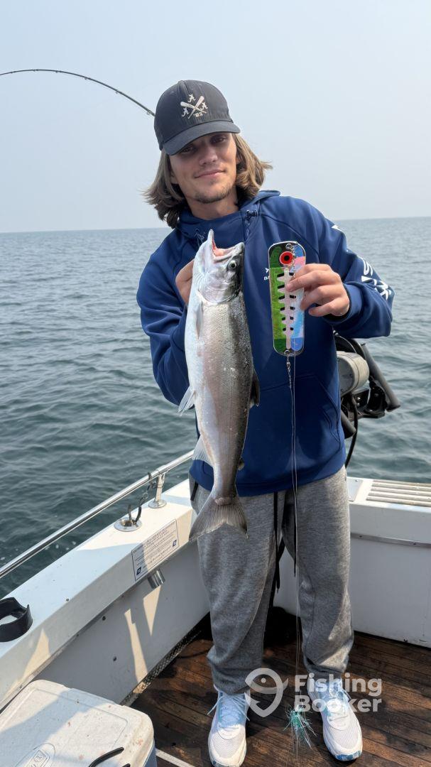 Young angler proudly holding a Silver Salmon while fishing from a boat in open waters.