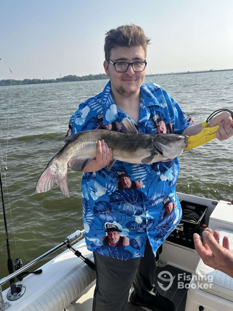 A young angler proudly displaying a large catfish while fishing on a sunny day, showcasing a vibrant fishing environment.