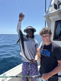 A young angler and a fishing guide proudly displaying a large fish on a sunny day at sea, showcasing a successful fishing trip.