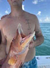 An angler proudly displaying a vibrant Red Snapper while fishing in clear blue waters.