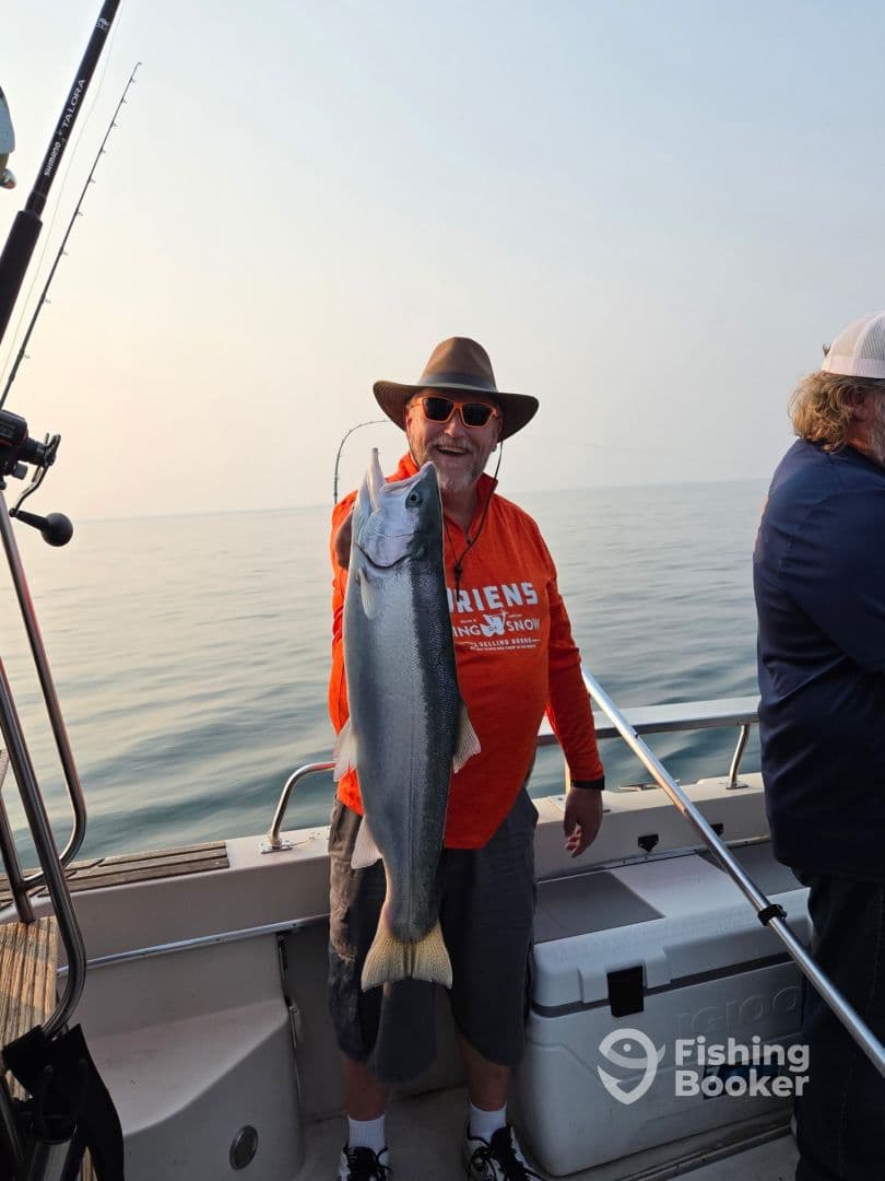An angler proudly displaying a large Salmon while fishing on a calm lake, showcasing a successful catch during a charter trip.