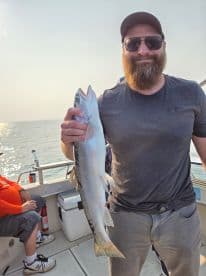 An angler proudly displaying a freshly caught fish aboard a fishing boat, enjoying a sunny day on the water.