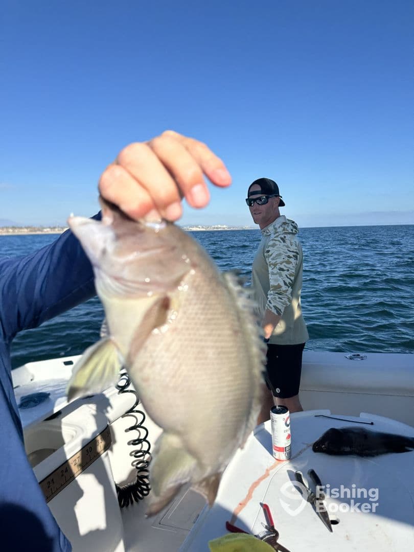 An angler proudly displaying a freshly caught fish while enjoying a day on the water, with another person visible in the background.