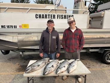 Two anglers proudly displaying their catch of several Salmon on a table in front of a charter fishing boat.
