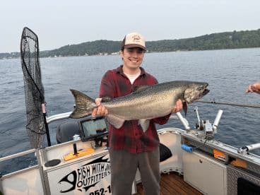 A young angler proudly displaying a large Salmon while fishing on a lake, showcasing a successful outing with Fish With Jim Outfitters.