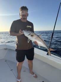 Angler holding a Silver Snapper on a fishing boat during a sunny day at sea.