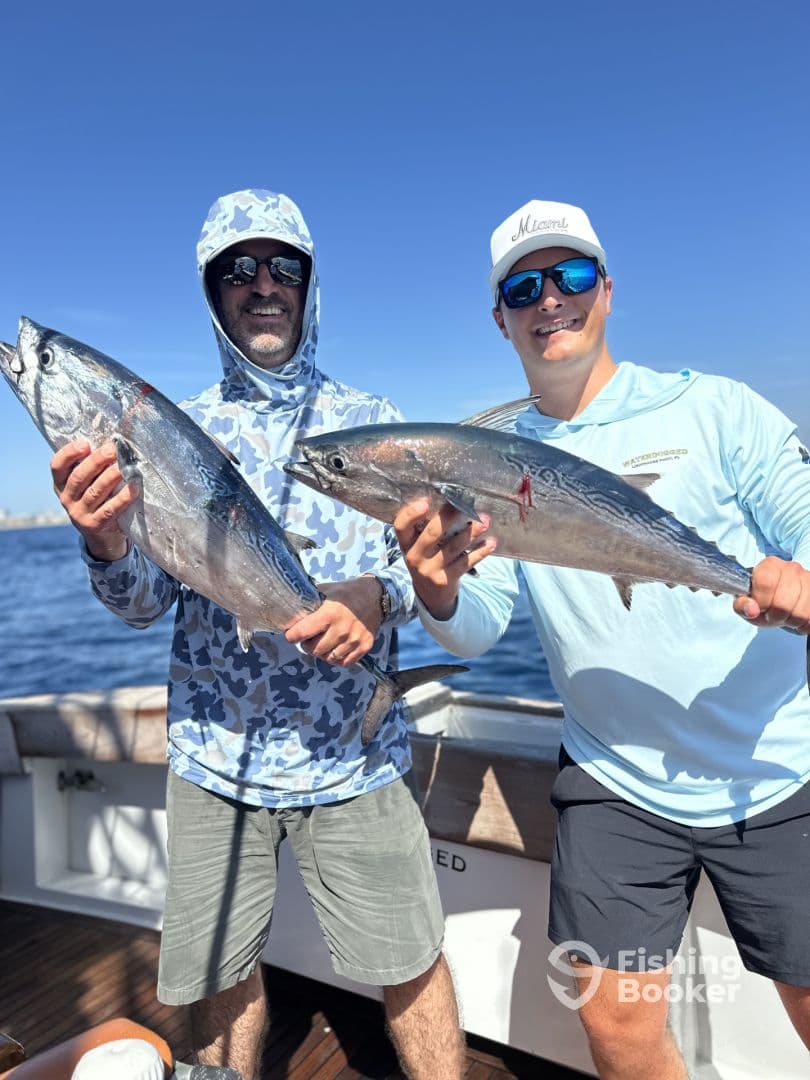 Two anglers proudly displaying their catches of fresh Tuna aboard a fishing charter in clear blue waters.