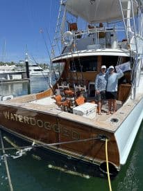 Two anglers posing on the deck of the 'Waterdogged' boat at the marina, showcasing its sleek design and fishing gear.