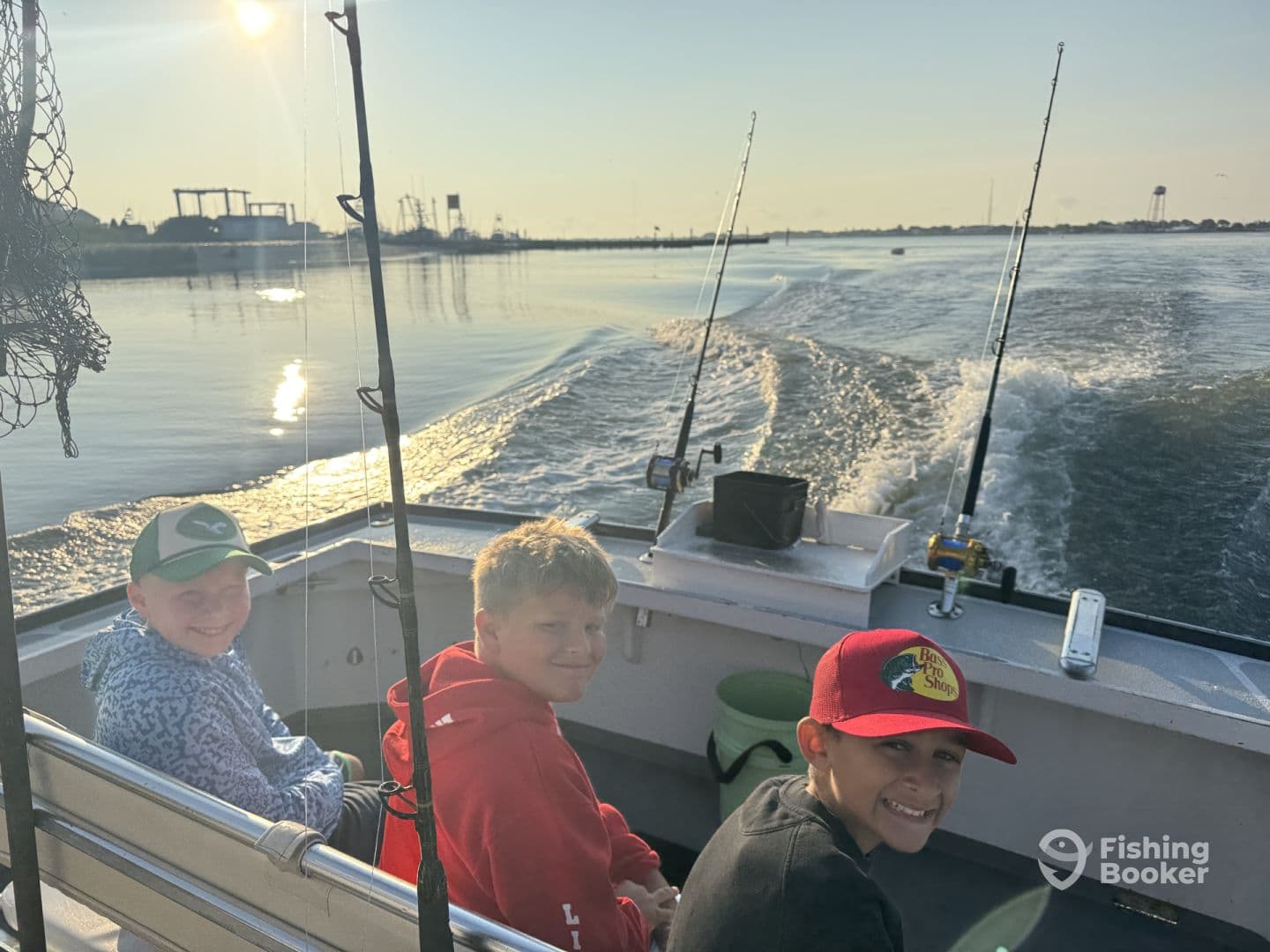 Three young anglers enjoying a morning fishing trip on a boat, with fishing rods ready and a scenic waterway in the background.