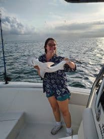 An angler proudly displaying a caught shark while aboard a boat, enjoying a fishing trip on open waters.