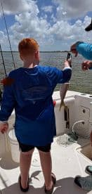 A young angler proudly displaying a caught fish while fishing on a boat, showcasing a sunny day on the water.