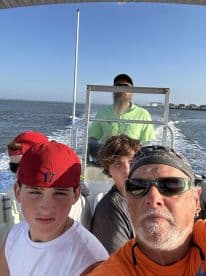 A group of anglers, including minors, enjoying a boat ride on a sunny day, with the captain navigating the waters.