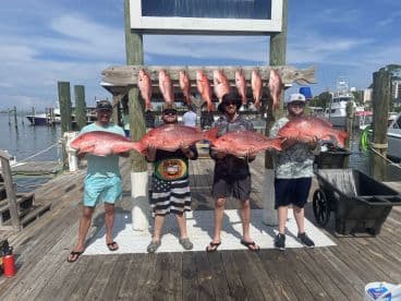 Four anglers proudly displaying their large Red Snapper catch at the dock after a successful fishing trip.